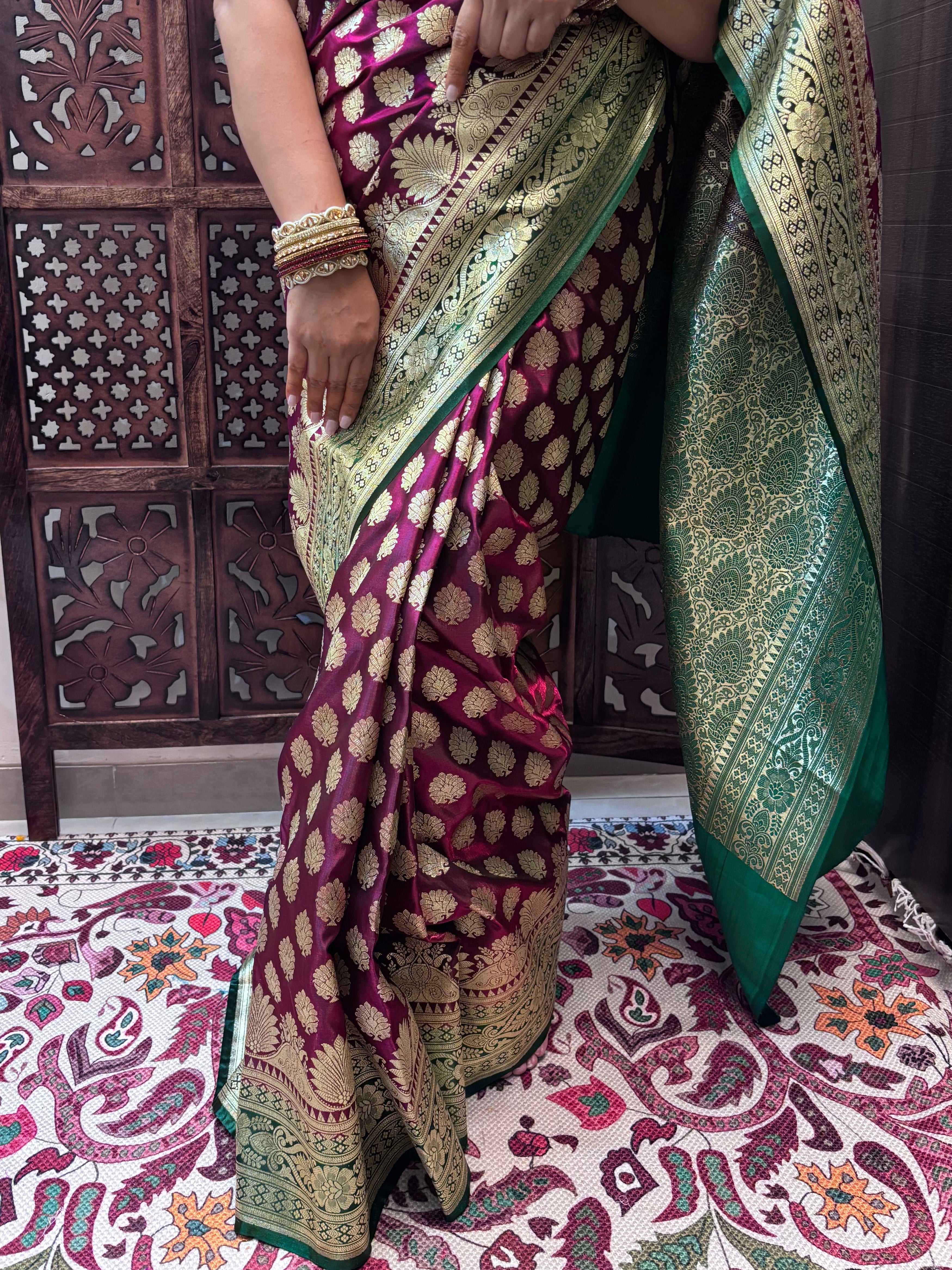 Person wearing a traditional saree with intricate patterns in a room with decorative walls.